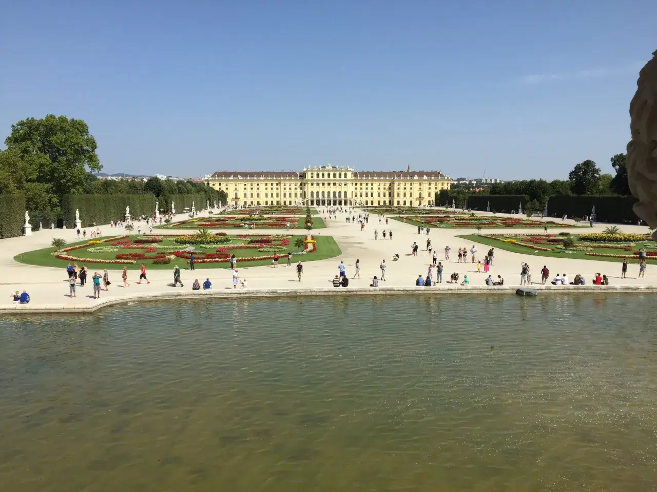 Wiedeń w jeden dzień: Pałac Schönbrunn i jego ogrody, z turystami spacerującymi pośród kwiatowych rabat i przy stawie.