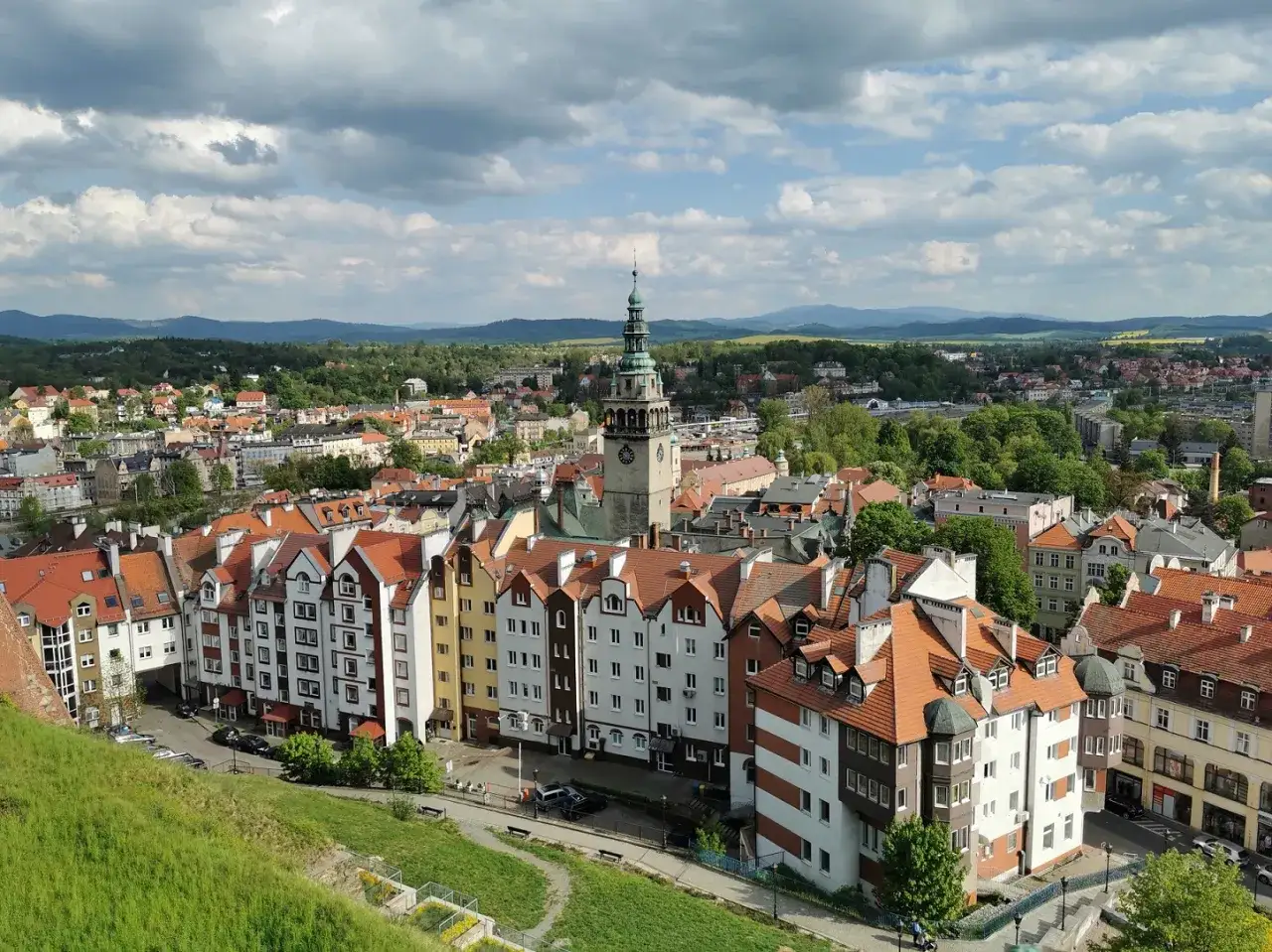 Widok na kłodzko stare miasto z wieżą ratuszową i kolorowymi kamienicami. W tle zielone wzgórza.