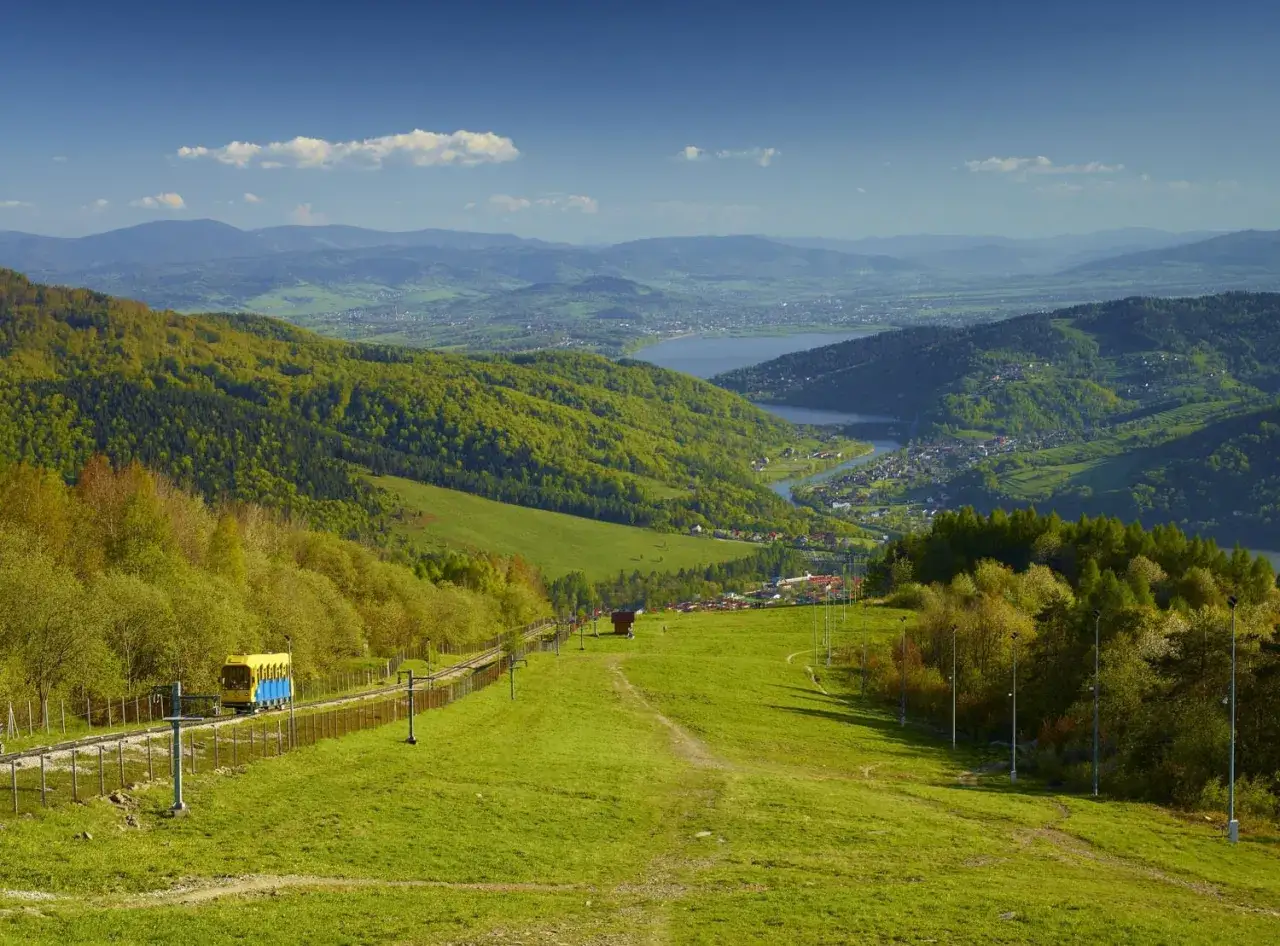 Widok na Beskid Mały z kolejką g&oacute;rską i jeziorem w oddali.