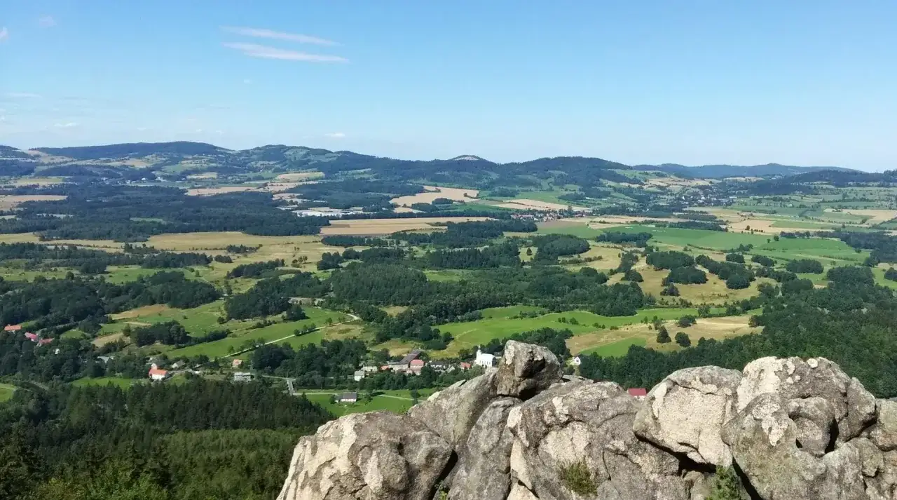 Krajobraz z punktu widokowego na Janowice Wielkie. W oddali widać pag&oacute;rki, pola i lasy, a bliżej zabudowania i kości&oacute;ł.