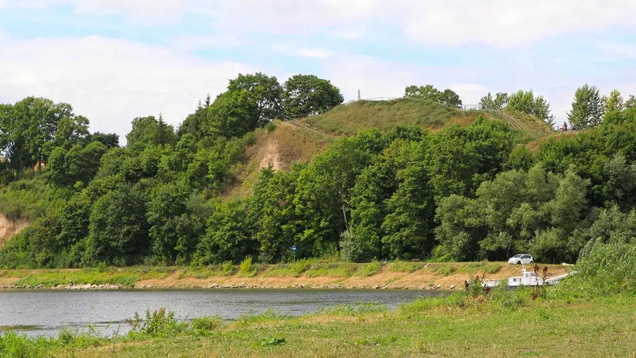 Zielona skarpa nad rzeką, na której wznosi się góra zamkowa w Drohiczynie. Widoczne schody i fragmenty ogrodzenia.