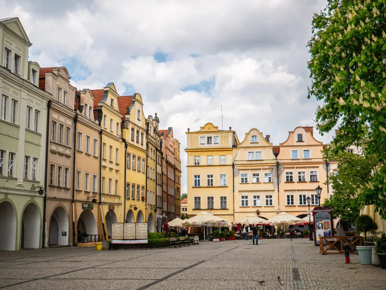Kolorowe kamienice na rynku w Jeleniej Górze, z arkadami i kawiarnianymi ogródkami.