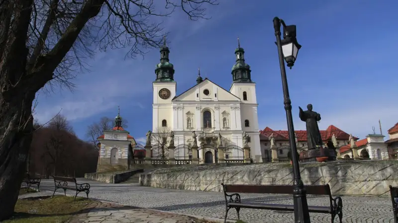 Kalwaria Zebrzydowska zwiedzanie: barokowy kościół z wieżami, kapliczki, ławki i pomnik.